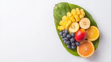 A vibrant arrangement of fresh mango, banana, , blueberries, and orange slices artfully displayed on a large green leaf against a bright white background. photo