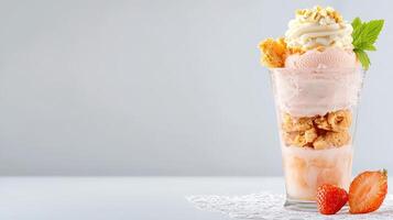 A refreshing strawberry ice cream sundae is layered with crunchy crumble and whipped cream in a tall glass perfect for a hot summer day. photo