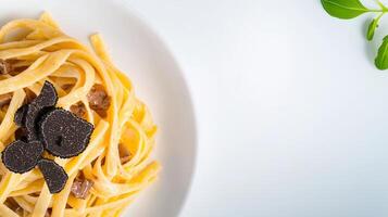 A delectable plate of creamy tagliatelle pasta is elegantly presented with gourmet black truffle slices atop the rich sauce on a pristine white plate. photo