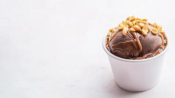 A delicious scoop of chocolate ice cream topped with caramel and peanuts sits in a small white cup against a bright white background perfect for dessert menus or food blogs. photo