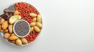 A white plate holds chia seeds, almonds, goji berries, and dark chocolate pieces arranged aesthetically on a bright white background offe a healthy snack option. photo