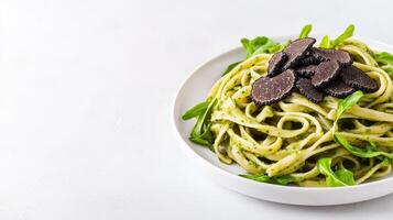A delectable plate of gourmet pasta linguine tossed in vibrant pesto sauce is elegantly garnished with fresh arugula and thin slices of luxurious black truffles. photo