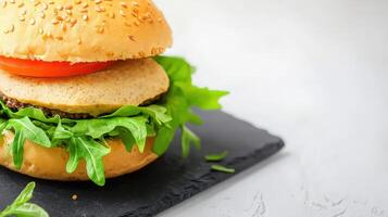 A delicious vegetarian burger with a flavorful patty sits on a dark slate serving board garnished with fresh arugula and tomato slices ready to be enjoyed. photo