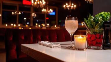 A romantic candlelit dinner for two is set on a pristine white table in a dimly lit upscale restaurant with a glass of chilled water and fresh salad. photo