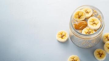 Delicious and healthy chia seed pudding with banana slices and peanut butter in a glass jar on a light blue background perfect for a nutritious breakfast or snack. photo