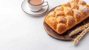 A freshly baked braided loaf of sweet bread rests on a rustic wooden board next to a warm cup of cocoa on a bright white background perfect for breakfast or a cozy afternoon treat. photo