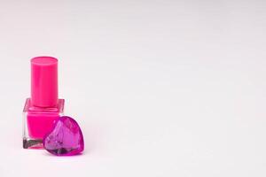 Pink nail polish with glass hearts of violet color on white background.Copy space. High quality photo