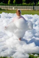 Child playing in foam outdoors on sunny day at foam party. photo