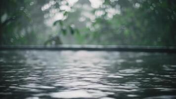 Rain falling on water creating ripples with blurred green foliage in the background outdoors video