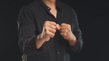 A man in a black shirt raised his fists while standing against a black background photo