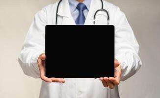 Doctor in uniform stands in a hospital holding a black tablet with a blank screen photo