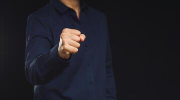 A man in a blue shirt raised his fist while standing against a black background photo