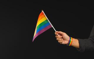 Close-up of a hand holding a rainbow flag showing in hand while standing against a black background. photo