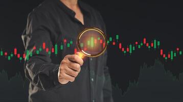 Stock exchange market analysis. Businessman or trader uses a magnifying glass to examine a stock graph on a virtual screen photo