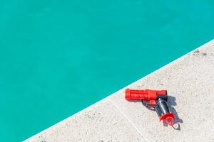 close view of a red and black toy gun near pool water, summer background concept photo