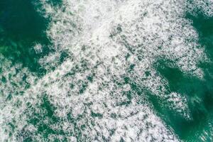 aerial perspective of foam of a dynamic breaking wave, top down view drone photography photo
