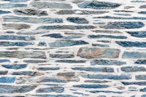 Flat blue-gray stones of various shapes are laid out on a rough wall, fastened with thick mortar joints, a textured background for design projects, photo