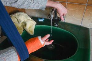 woman with broken arm in cast checks the temperature of the tap water for washing her hands, the concept of changes in the sensitivity of the limb after an injury, photo