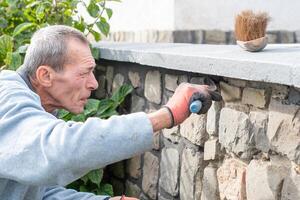 A builder carefully applies cement between the stones of a wall with a narrow trowel, restoring the appearance of a historic building using professional methods and tools photo