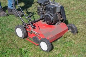 Gardener works with a scarifier, removing moss and thatch from a lawn, improving its health and appearance seasonal Gardening on a bright sunny spring day, photo