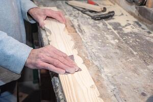 Close-up of carpenter's hands skillfully sanding decorative wooden plank on workbench in carpentry workshop, surrounded by various tools and small sawdust photo