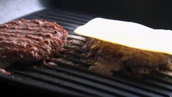 Close-up of juicy burger patties sizzling on a grill with melted cheese being added for a delicious meal video
