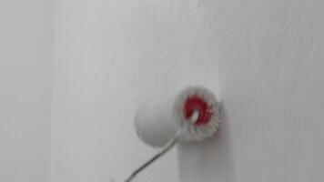 Close-up of a hand using a roller brush to paint a textured white wall, highlighting home improvement and renovation work. video