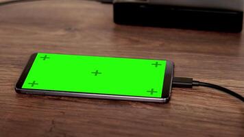 Close-up of a smartphone connected to a charger with a green screen display, emphasizing technology, charging, and digital devices. video