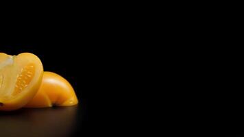 Close-up of fresh yellow cherry tomato half with smooth texture on black reflective surface in studio lighting video