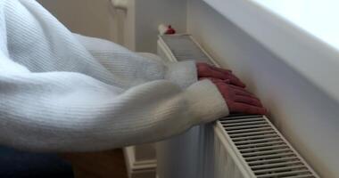 Close-up of a person warming their hands on a home radiator, emphasizing the need for warmth and comfort during cold weather. video