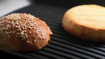 Close-up of golden sesame seed burger bun toasting on black grill pan in cozy kitchen setting video