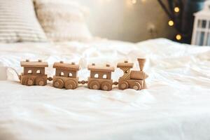 Wooden train toy displayed on a bed with soft textiles in a cozy room during daylight photo