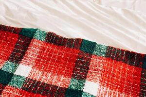 Cozy red and green plaid blanket draped over soft white bedding in a warm indoor setting photo