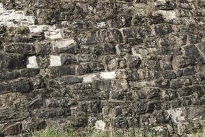Detailed view of historic stone wall with moss and grass at the base in sunny daylight photo