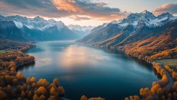 Snowy mountain peaks reflecting on lake during sunset with autumn foliage photo