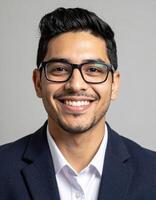 A young man with glasses smiles broadly in a business suit photo