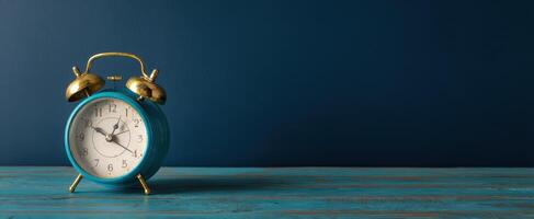 The vibrant blue alarm clock on wooden table against a dark background. photo