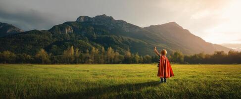 The child in a superhero cape stands triumphantly against majestic mountains. photo