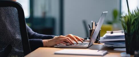 The hands typing on a laptop in a modern workspace with plant and documents. photo