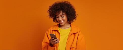 The woman smiling while using a smartphone against a vibrant orange background. photo