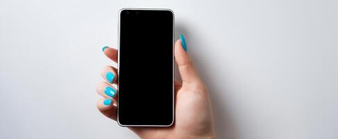 The smartphone held by a hand with stylish blue nails on a minimal backdrop. photo