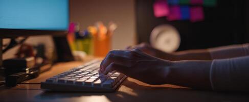The focused hands typing on a keyboard in a cozy workspace at night photo