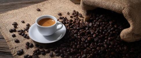 The espresso cup surrounded by freshly roasted coffee beans on burlap. photo