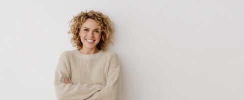 The smiling woman with curly hair poses confidently against a plain background. photo