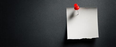 The simple red pushpin holding a blank note on a textured black background. photo