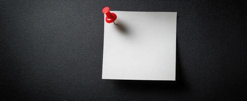 The red pushpin holding a blank note on a textured black surface. photo