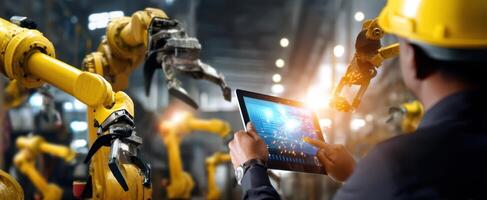 The worker monitoring robotic arms using a tablet in a modern factory environment. photo