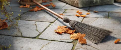 The broom resting on a weathered stone pavement surrounded by fallen leaves. photo