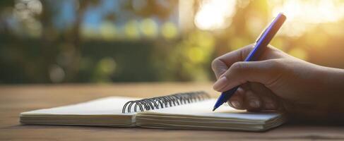 The hand holding a pen poised to write in a notebook outdoors. photo
