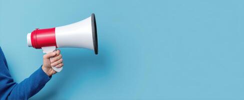 The megaphone held firmly by a hand against a blue background. photo